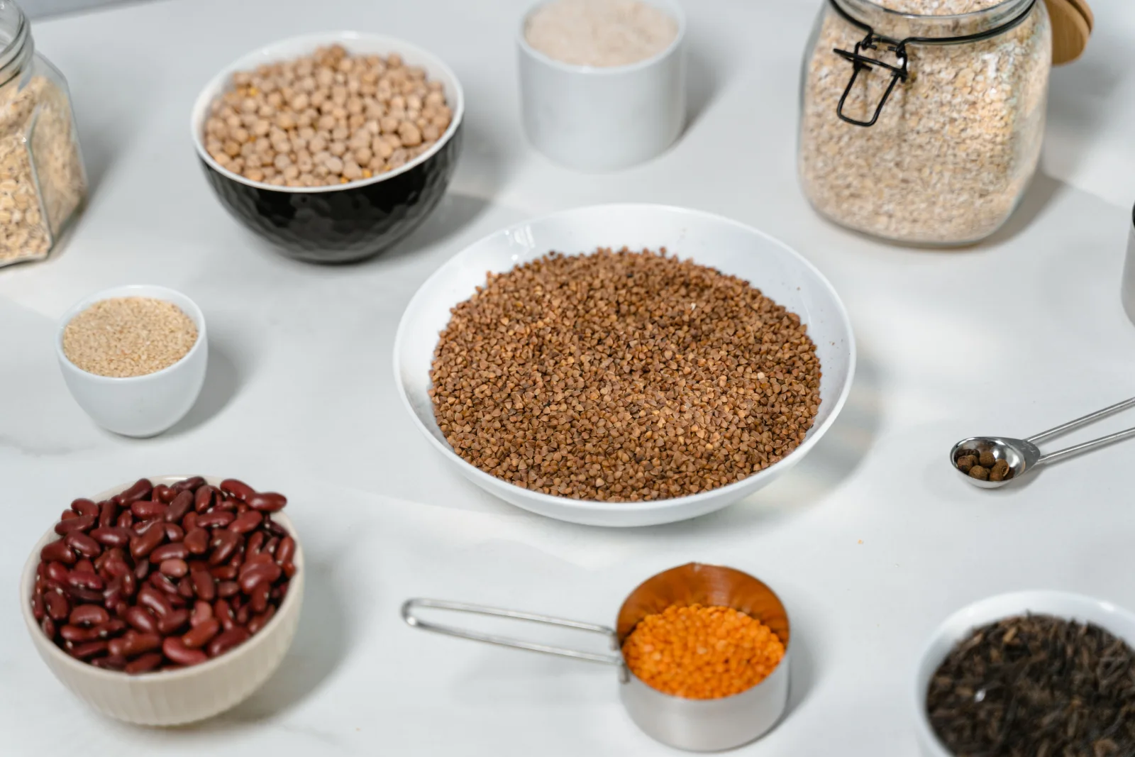 Bowls and jars of grains, chickpeas, beans and lentils arranged on a pale kitchen surface.