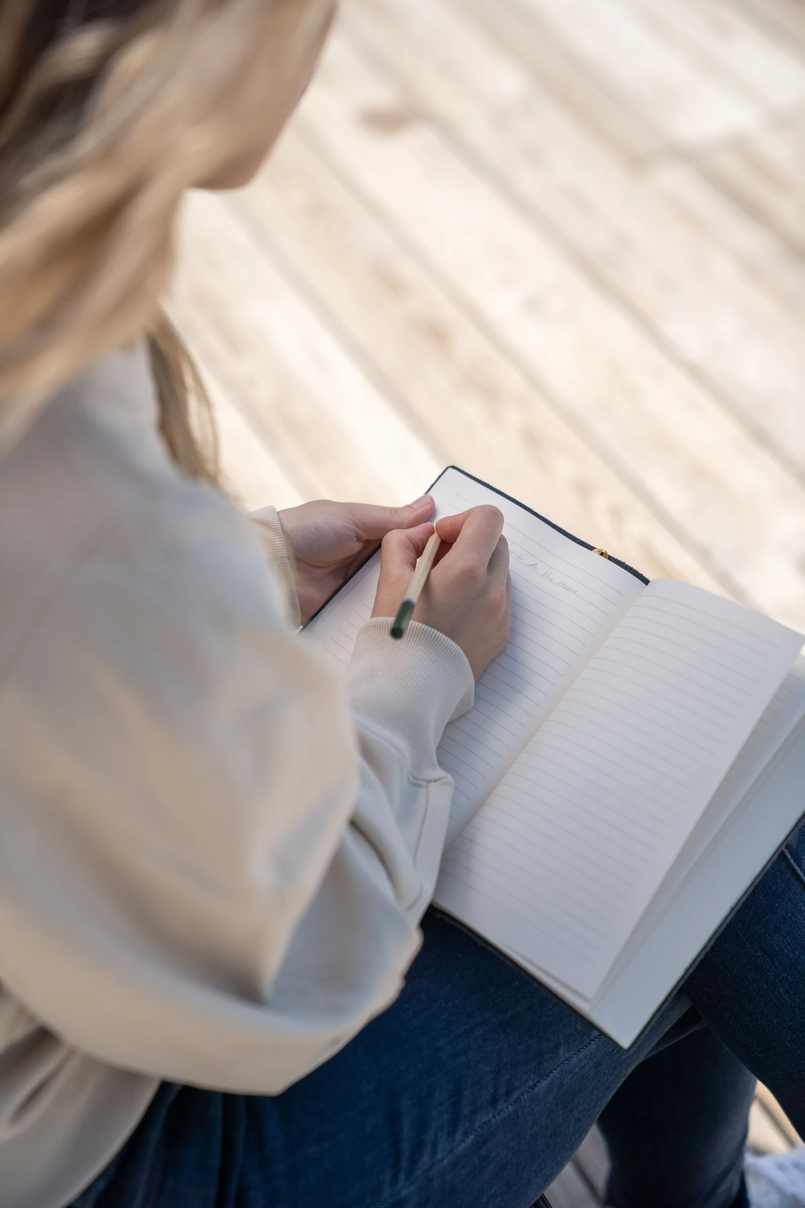 Hands writing in a lined notebook with a pencil.