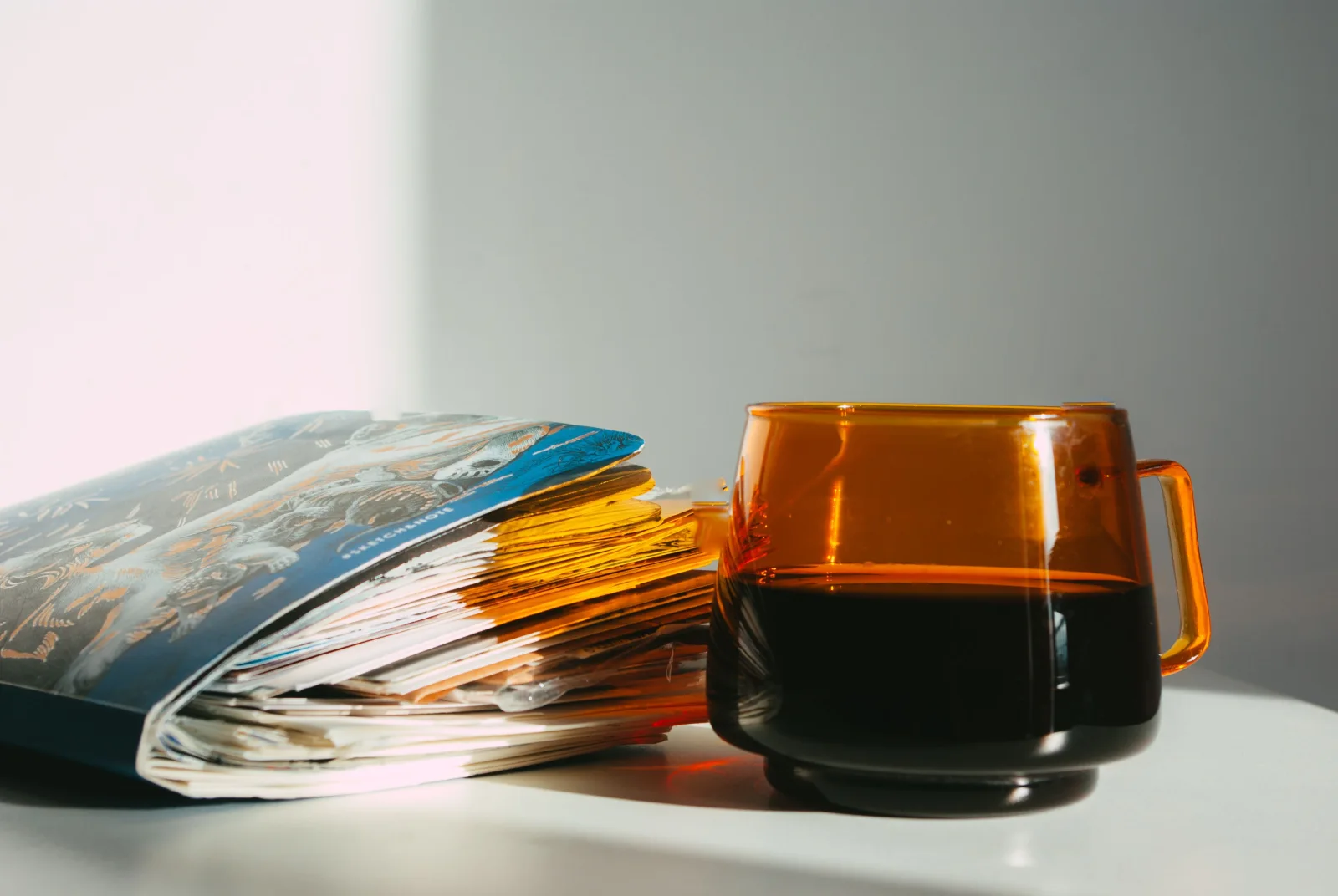An open journal beside an amber glass mug in sunlight.