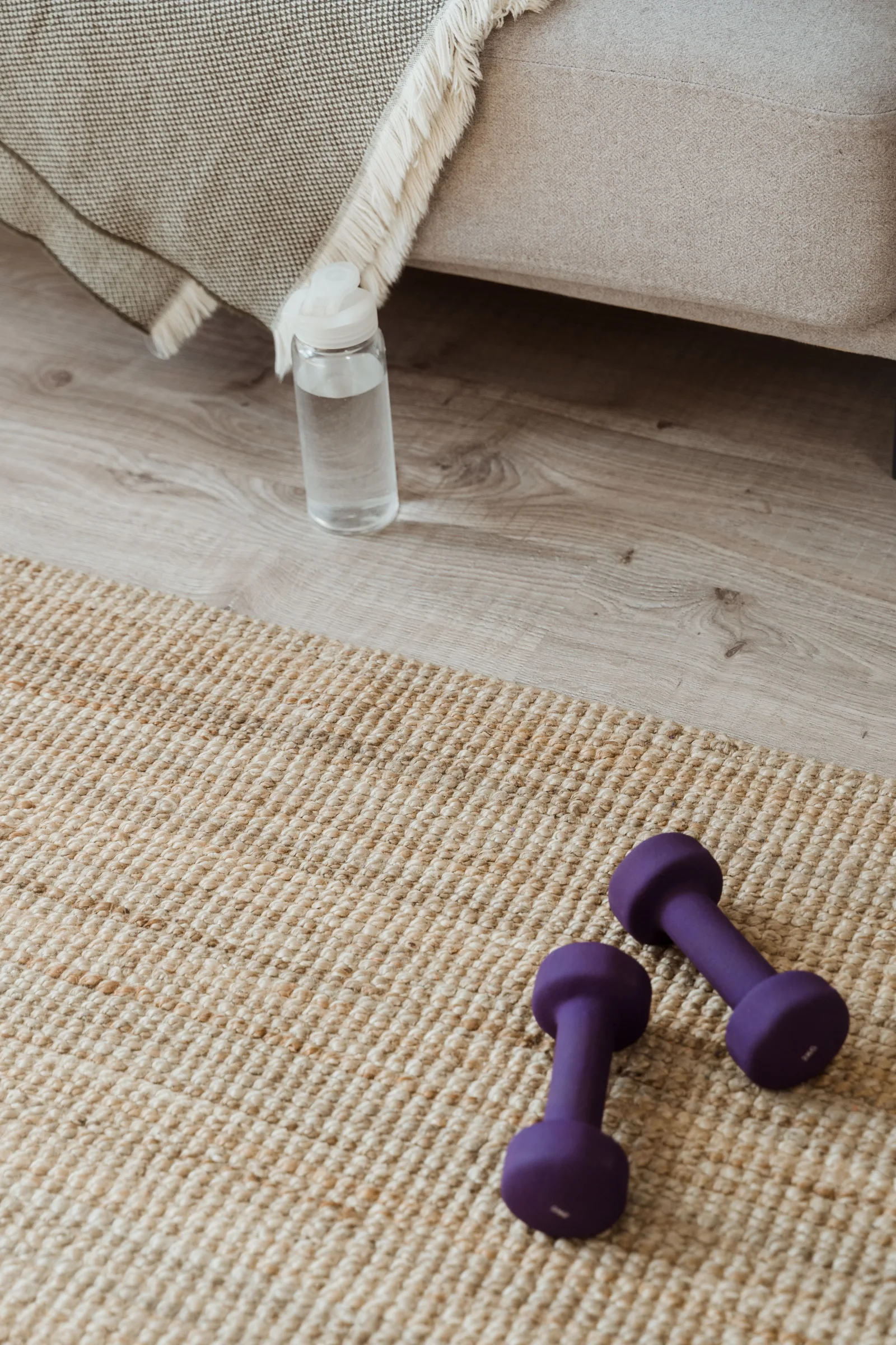 Purple dumbbells resting on a woven mat in a home exercise space.