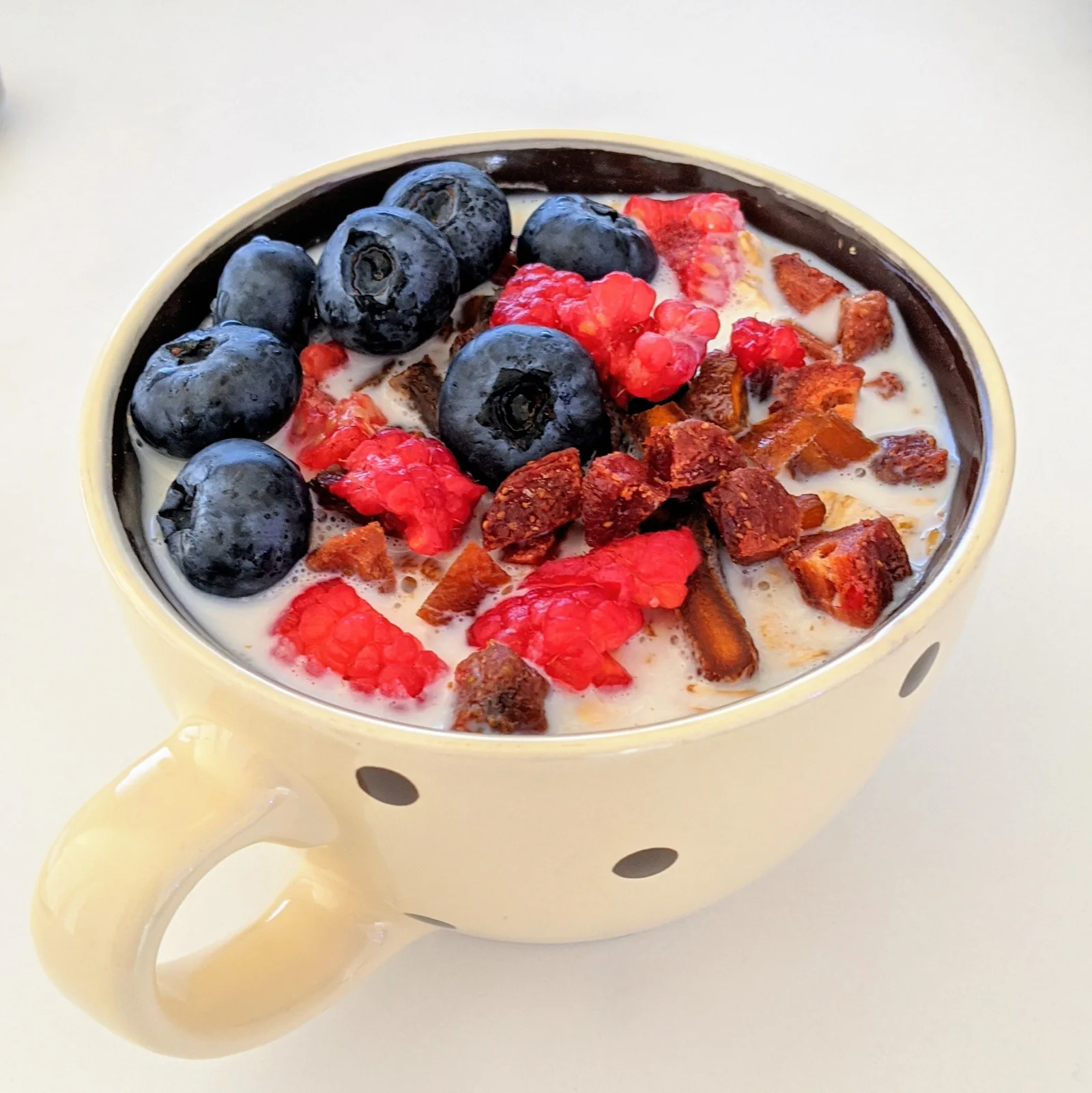 Yogurt topped with blueberries, raspberries and dried fruit in a ceramic cup.