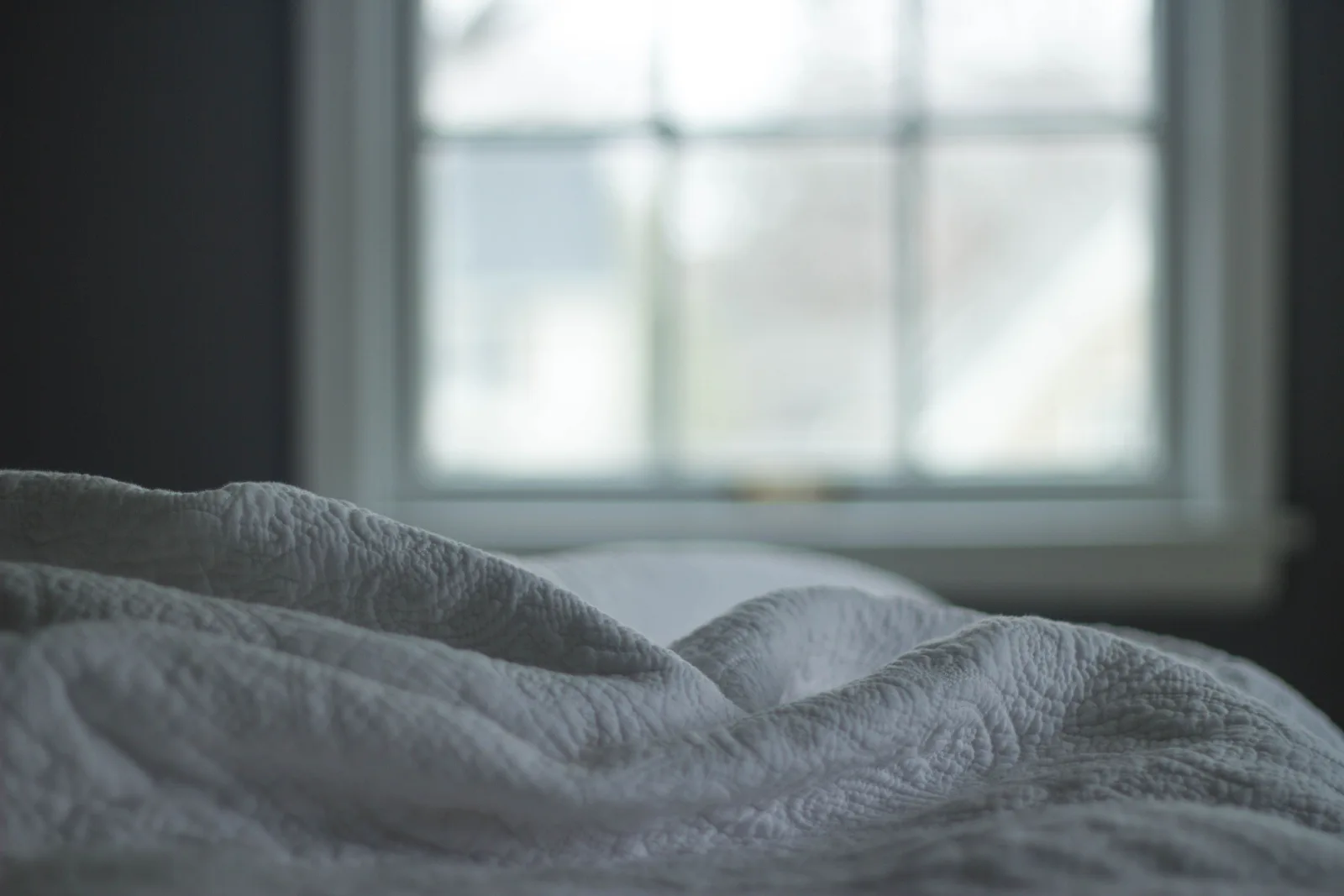 White quilted bed linen in soft natural light beside a bedroom window.