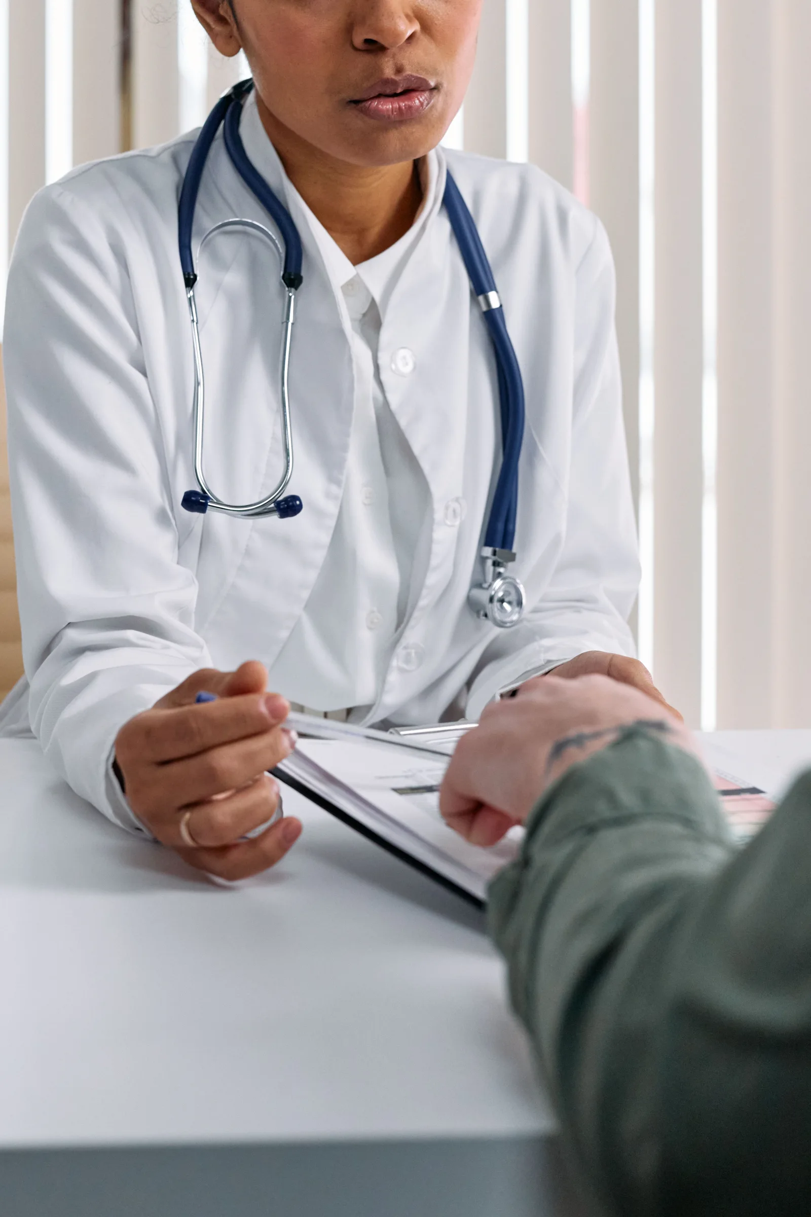 A stock consultation photograph showing a clinician's hands, stethoscope and paperwork across a table.