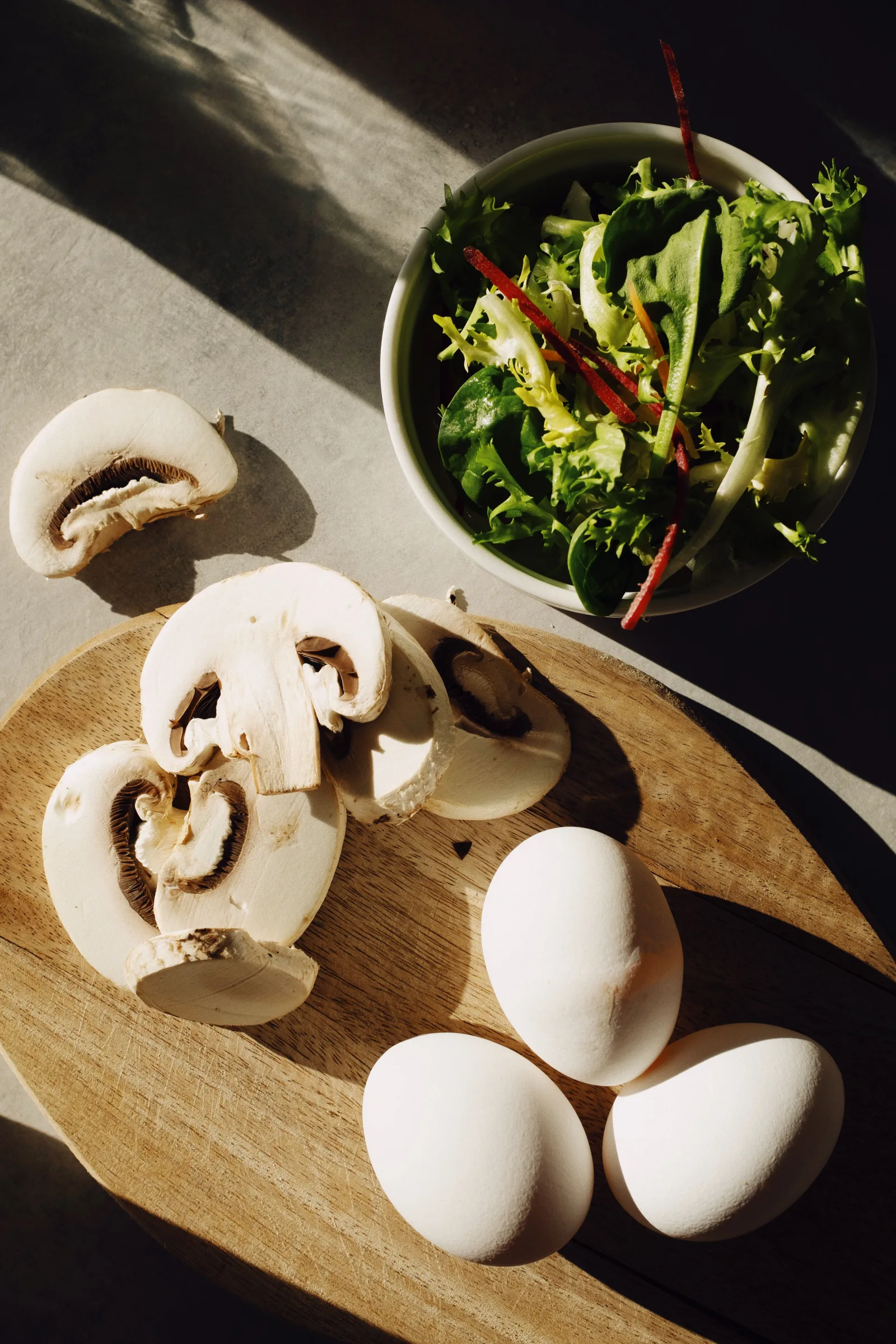 Mushrooms, eggs and salad greens arranged in natural light on a wooden board.